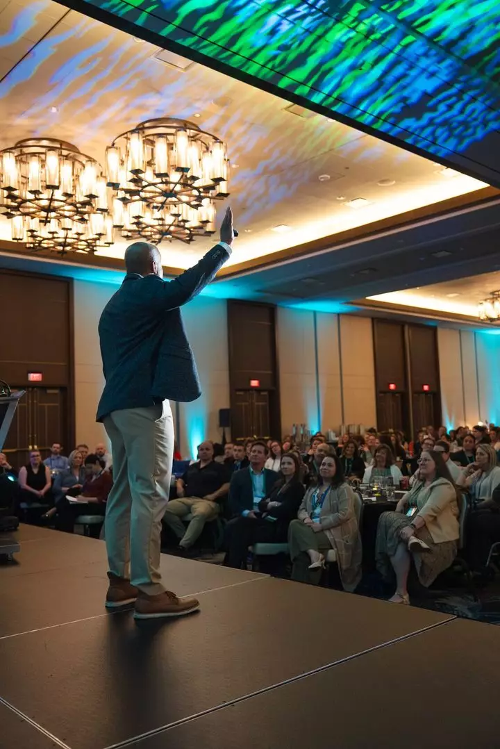 A keynote speaker on stage addressing a full ballroom at the 2026 Summit